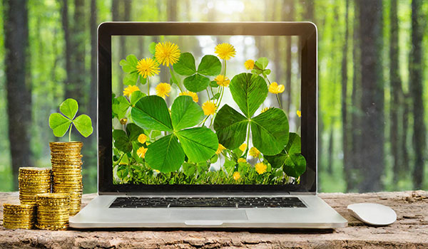 begagnad laptop på bänk med guldpengar och fyrklöver